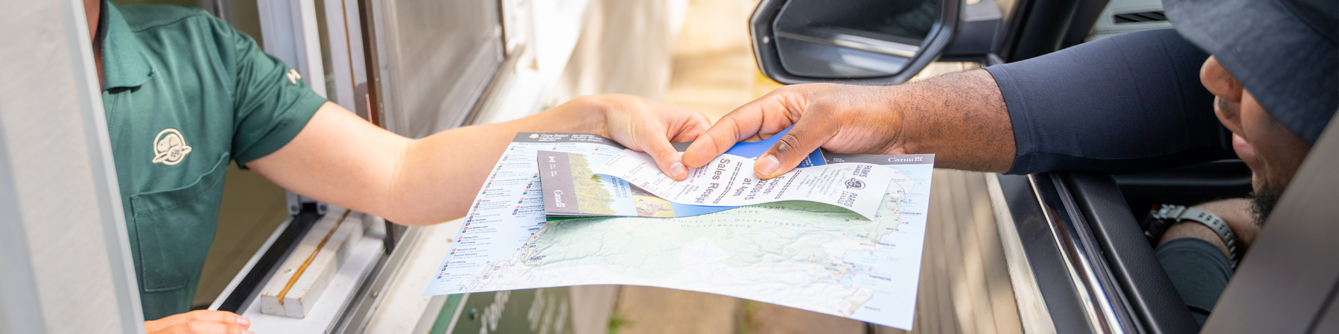 A person hands a receipt to a visitor in a car at the entrance gate to Cape Breton Highlands National Park