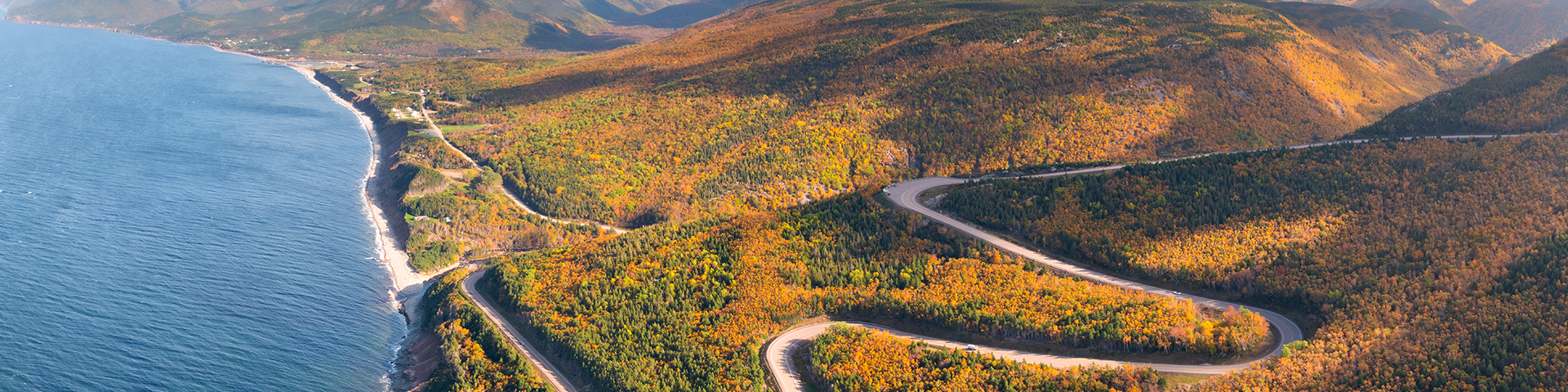 Vue aérienne de la Cabot Trail serpentant à travers un feuillage automnal jaune, orange et rouge.