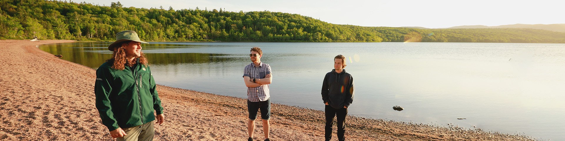 A guide chats with two visitors on a sandy beach at sunset.