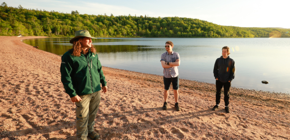 Un guide discute avec deux visiteurs sur une plage de sable au coucher du soleil.