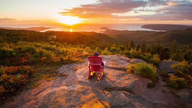 Une personne assise sur une chaise rouge regarde le lever du soleil surplombant l’océan Atlantique.