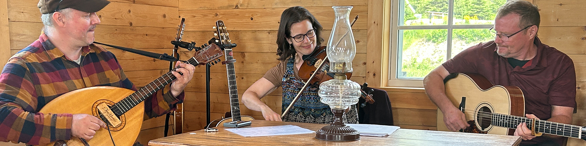 Three people sitting at a table playing guitars and a fiddle.