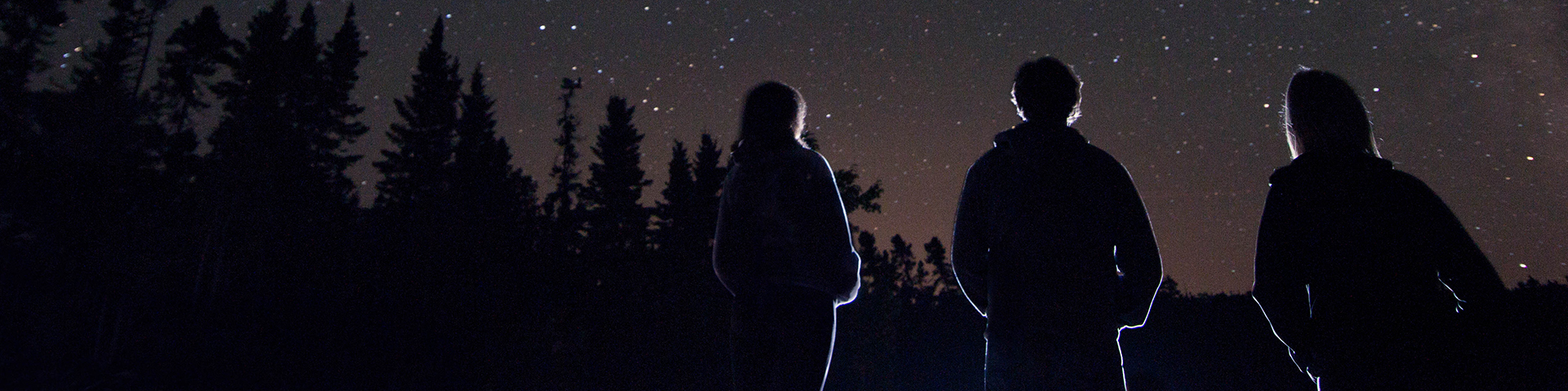 Three people standing together gazing at the night sky full of stars.