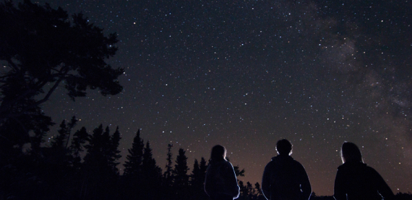  Three people standing together gazing at the night sky full of stars.