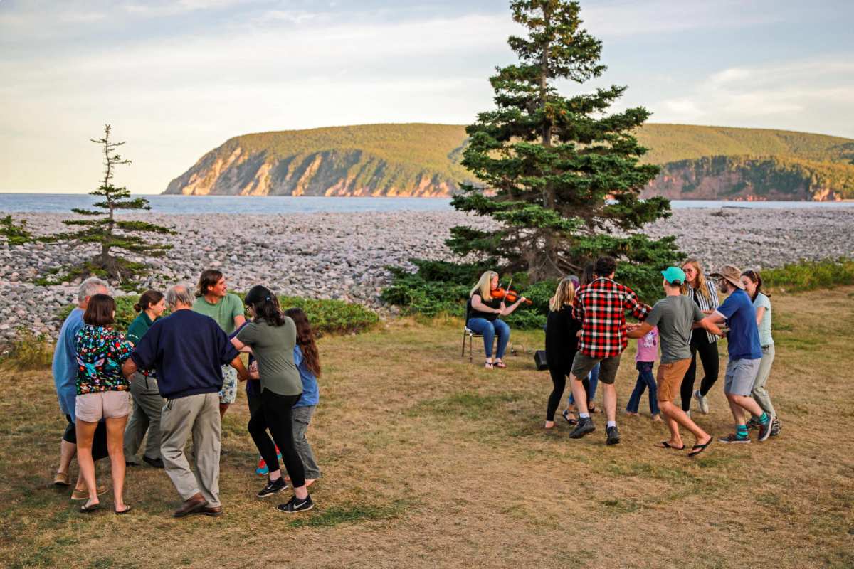 Un grand groupe de visiteurs dansent la danse carrée d’Ingonish au son du violon à l’aire de fréquentation diurne du Lac-Freshwater.