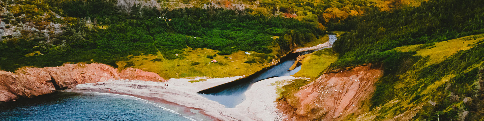 Photo aérienne d'une anse avec des tentes nichées dans l'herbe et les arbres au bord d'une rivière, à côté de l'océan.