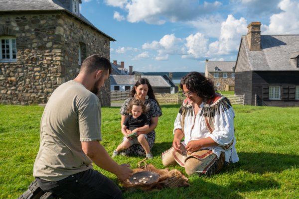 Visitors sitting on the grass with a Mi’kmaq interpreter, playing Waltes.