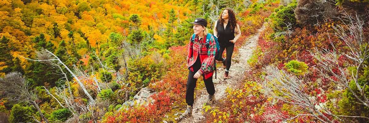 Deux femmes souriantes se promènent sur un sentier entouré de feuilles d'automne lumineuses.