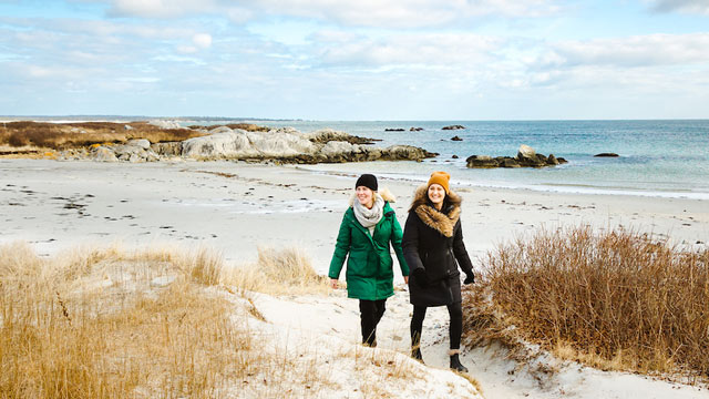 Two people in winter coats walk on the beach.