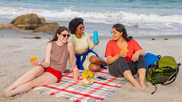 Three people picnic on the beach.