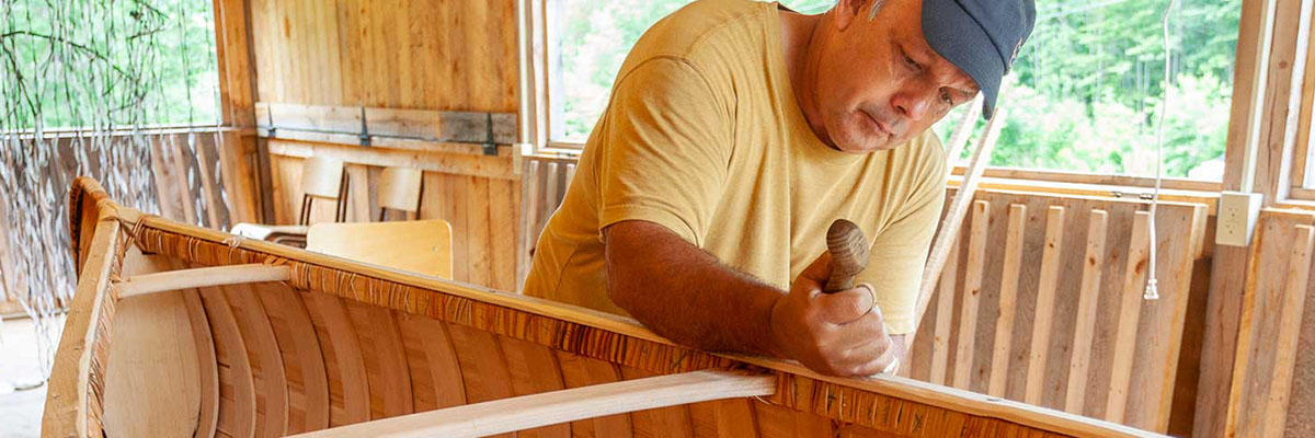Todd using a tool on the top of the canoe.