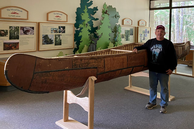 Todd Labrador next to a birchbark canoe inside a room.