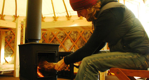 A man starting a fire inside the woodstove in the centre of the wood and canvas yurt.
