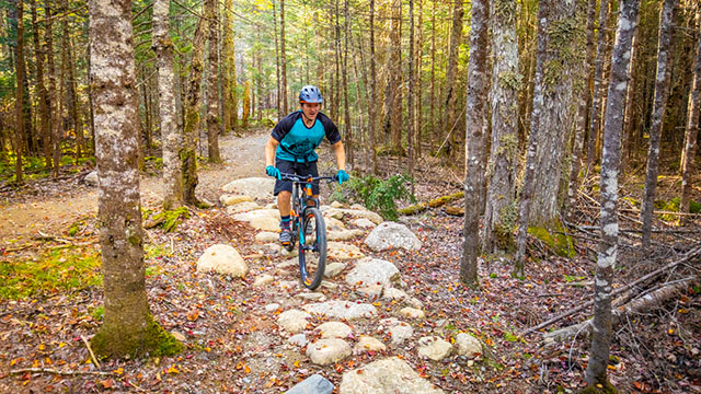 Un cycliste roule sur une section de sentier recouverte de grosses pierres.