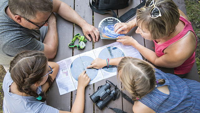 Un groupe de personnes est assis à une table de pique-nique et consulte une carte du ciel.
