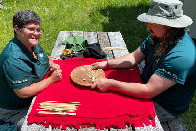 Two people play a game with small pieces on a wooden plate at a table.
