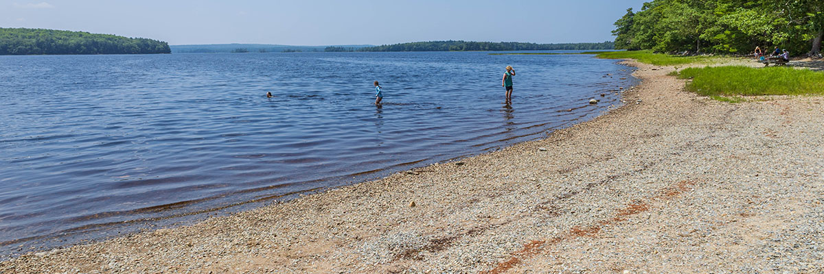 Trois personnes profitent de l’eau et d’une plage de sable.