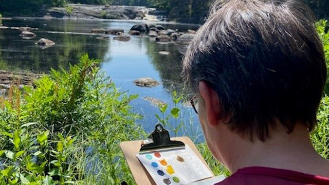 A person painting a picture next to the water.