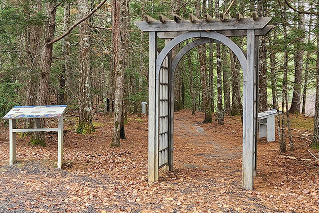A wooden arbour over the gravel path that is covered with leaves.