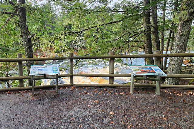 A wooden guard rail and information panels next to Mill Falls.