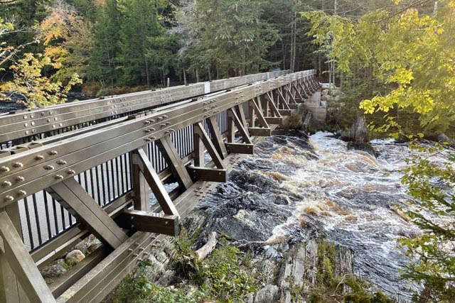 Un pont en acier enjambe une partie rocheuse et rapide de la rivière.