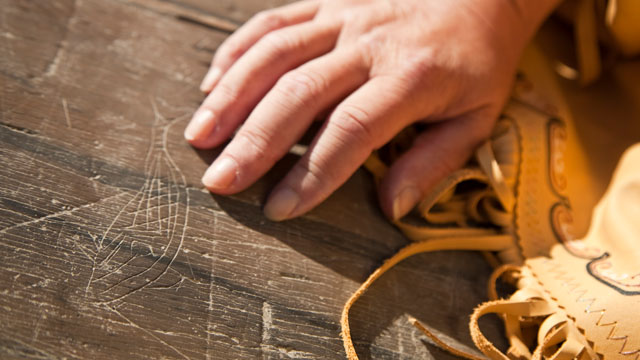 Une main touchant des pétroglyphes sculptés dans la pierre.
