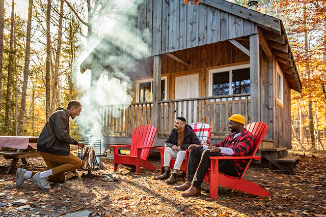Three friends enjoy a campfire at a rustic cabin.