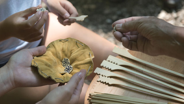 Mains tenant des pièces de jeu en os, en cuir et en bois.