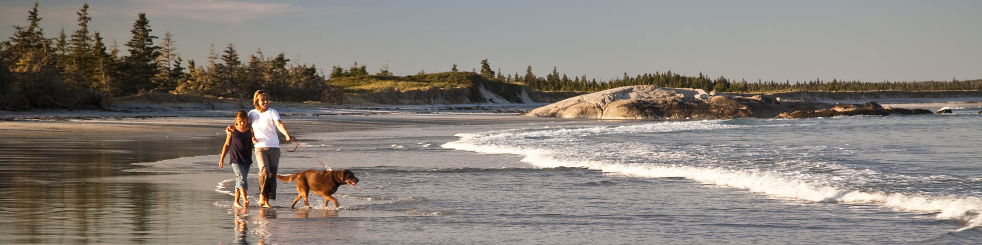 A family enjoys a walk on the beach at Kejimkujik Seaside.