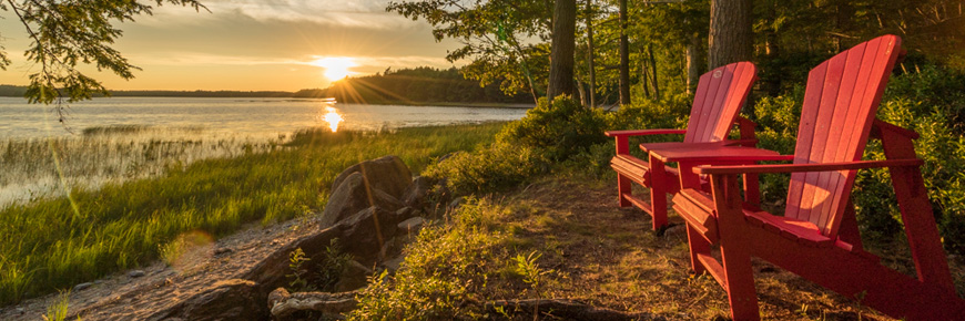 Les chaises rouges de Parcs Canada au bord d'un lac avec le coucher du soleil