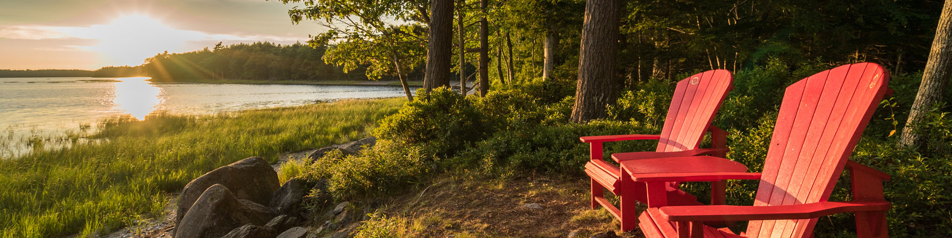 Les chaises rouges de Parcs Canada au bord d'un lac avec le coucher du soleil