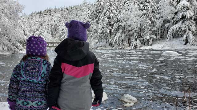 Des arbres couverts de neige et deux enfants vêtus pour l’hiver.