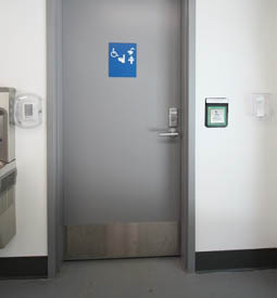 A sign with braille and a push-button operated door to access the family accessible washroom, including toilet and change table.