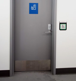 A sign with braille and a push-button operated door to access the accessible shower. 