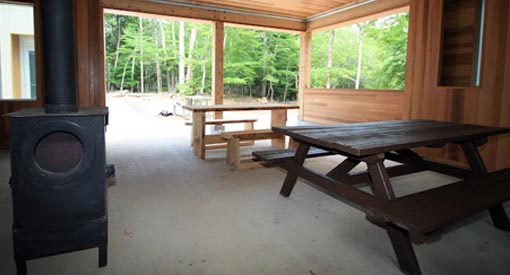 Picnic shelter at Jim Charles Point with two picnic tables, a wood-stove, seating benches, and prep table.