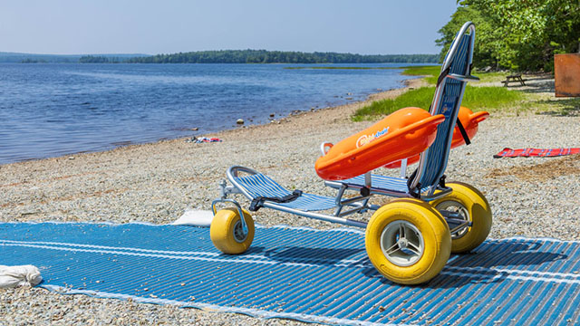 Un fauteuil de plage amphibie sur un tapis de mobilité sur la plage.