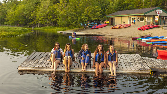 Cinq personnes portant des gilets de sauvetage sont assises sur le quai à côté du bâtiment Whynot Adventure.