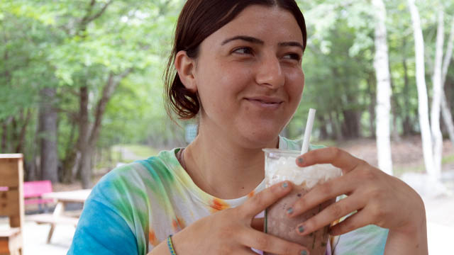 A smiling person drinking a milkshake outside.