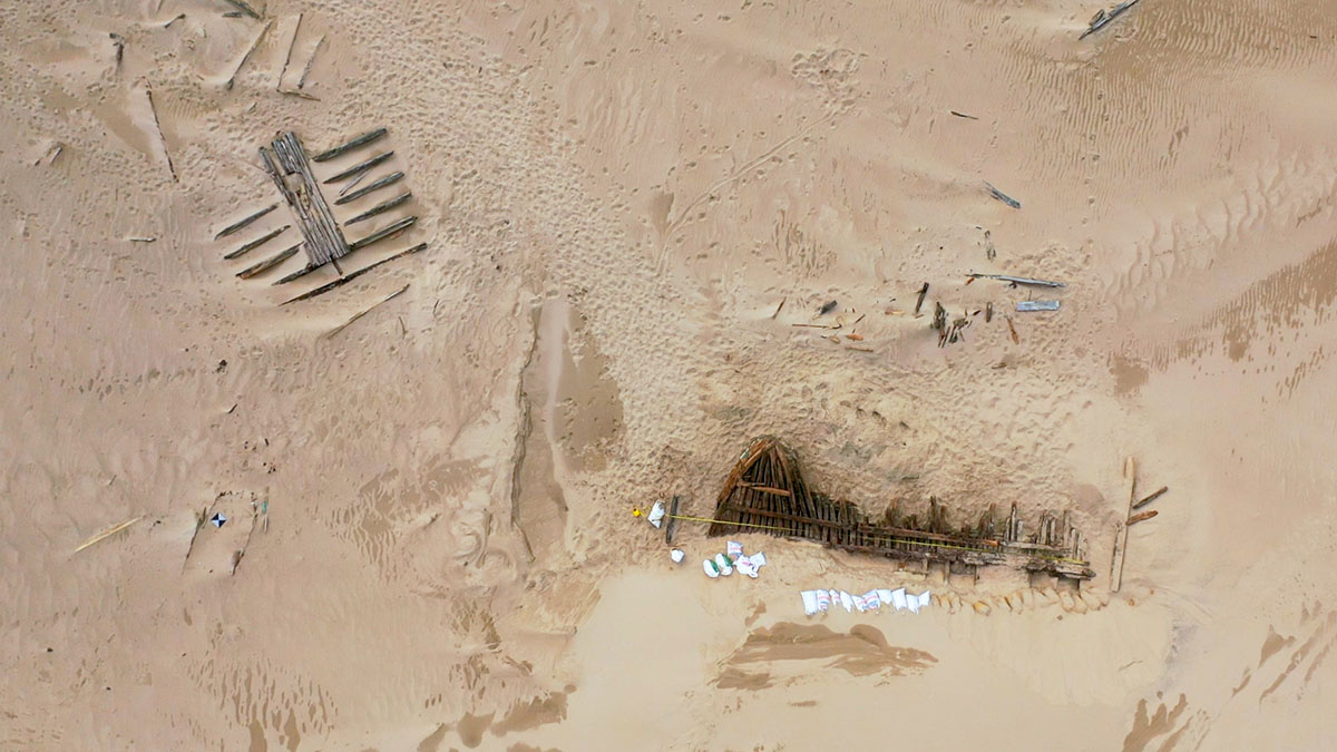 An aerial view of the dig site, with one wreck section exposed and one wreck section partially covered by sand.