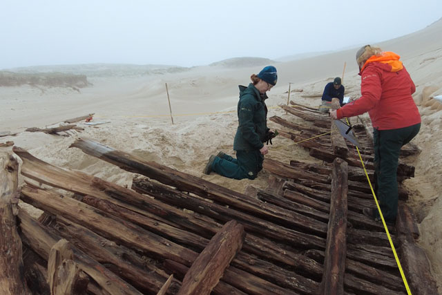 Three people work together to measure the wreck section with a measuring tape.