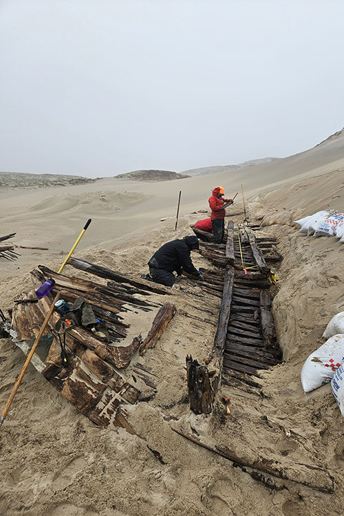 Two people measuring and recording details of the wreck section on paper.