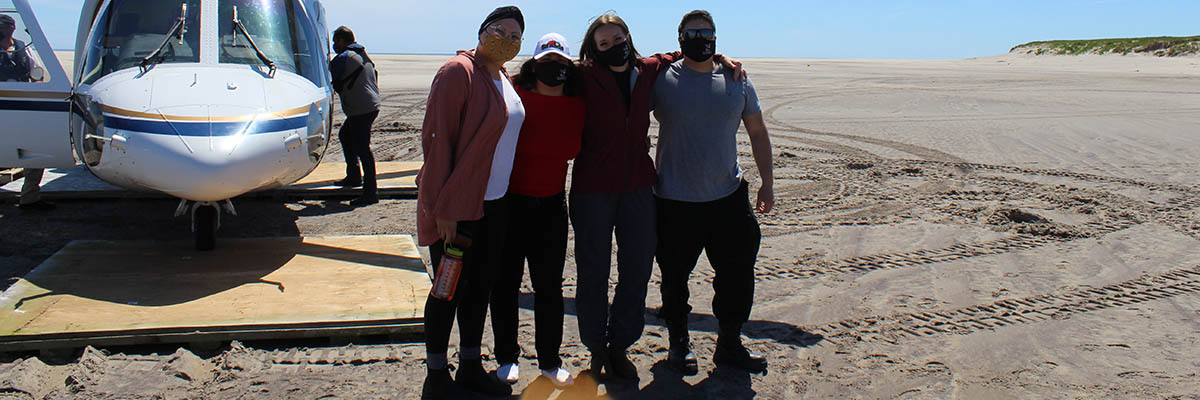 Four people pose in front of a helicopter on Sable Island.