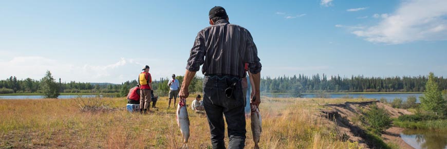 A person carrying two fish to a camp.