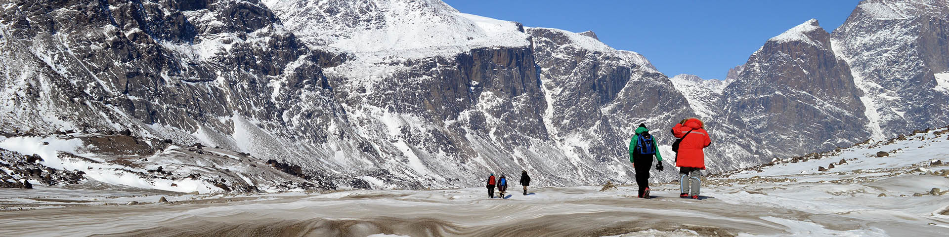 A group of people walking through a snowy mountainous landscape. 