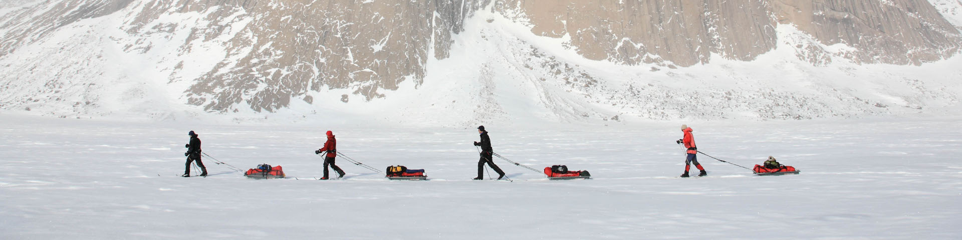 Four people skiing with pulk sleds in the Akshayuk Pass. 