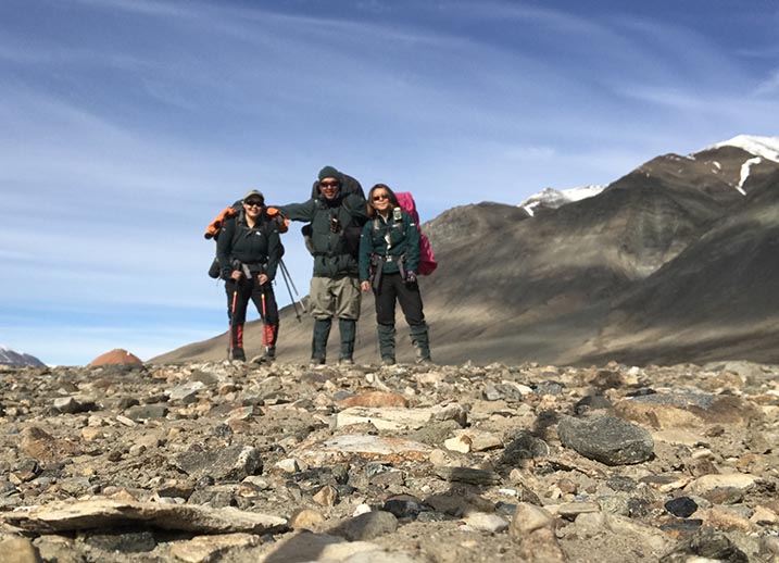 Three Parks Canada employees stand together on rocky terrain with mountains in the background.