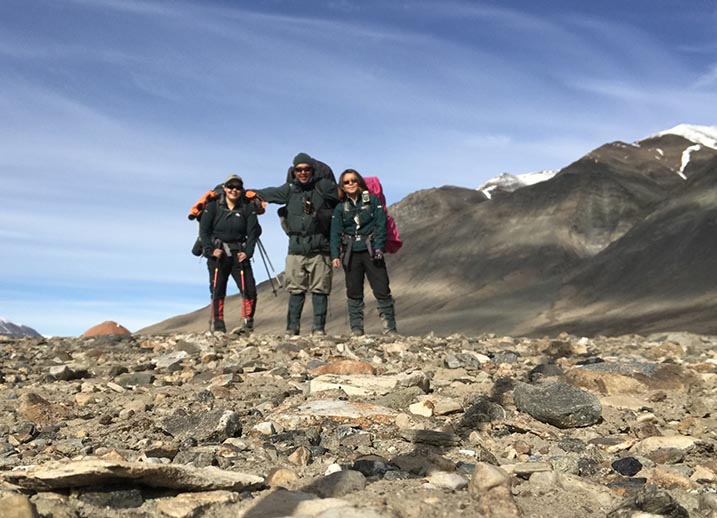 Three Parks Canada employees stand together on rocky terrain with mountains in the background. 