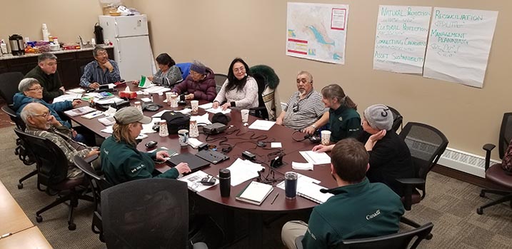 Des membres de la communauté et du personnel de Parcs Canada discutent autour d’une table dans une salle de conférences.