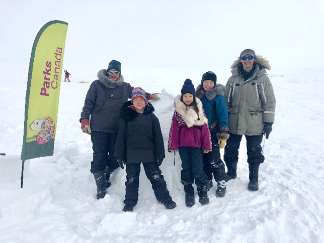 Two adults and three children standing in front of an igloo.