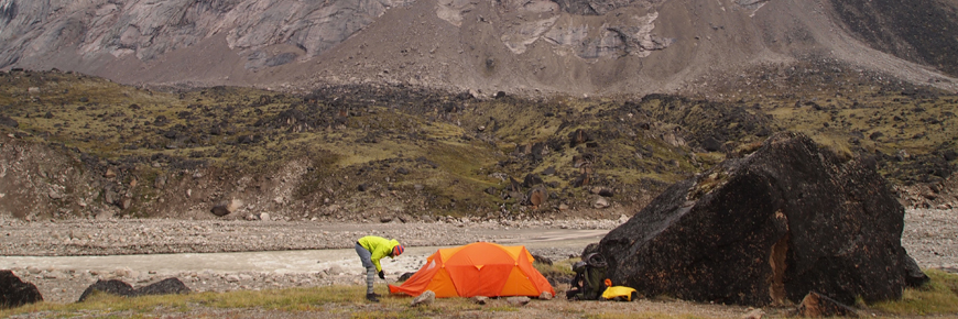 A person setting up an orange tent beside a boulder.